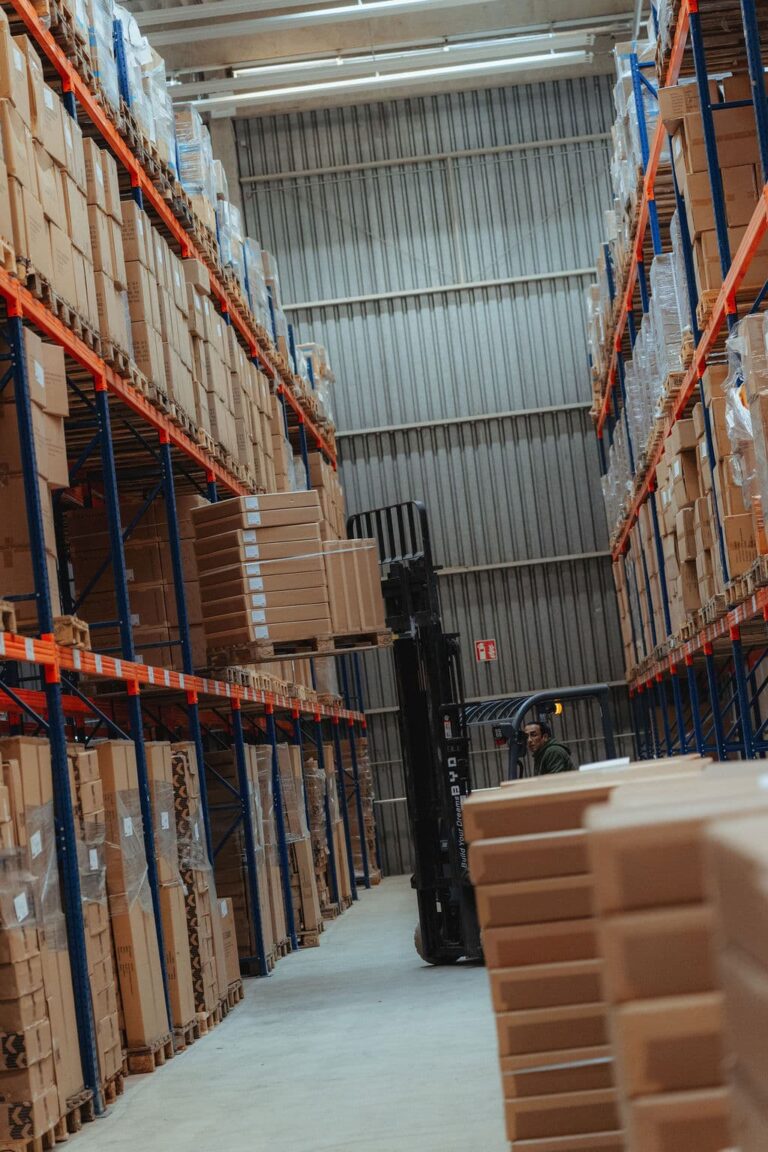 Ein Gabelstapler hebt eine Palette mit Kartons in ein hohes Lagerregal eines Logistikzentrums.