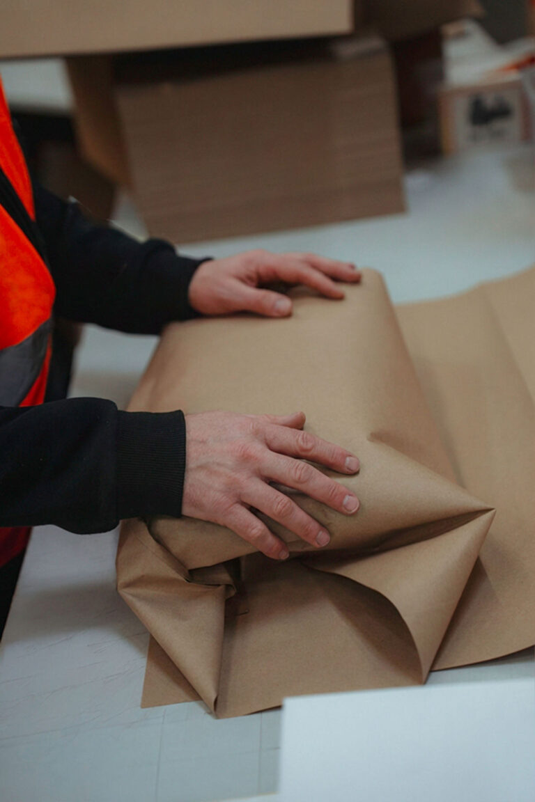 Hände schlagen hochwertige Textilien sorgfältig in weißes Seidenpapier ein.