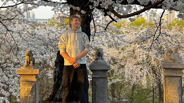 Ein Mann steht vor einem Baum mit weißen Blühten und lächelt.