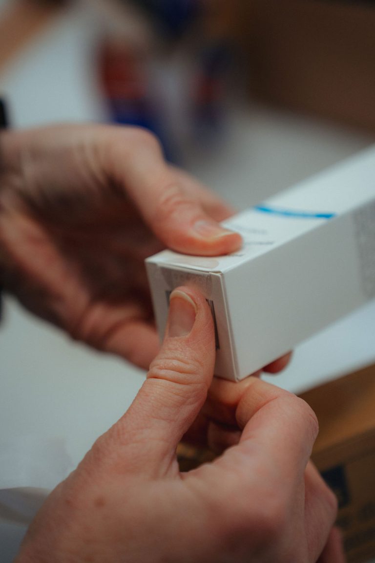 Hände versiegeln einen Kosmetikkarton mit einem durchsichtigen Aufkleber.