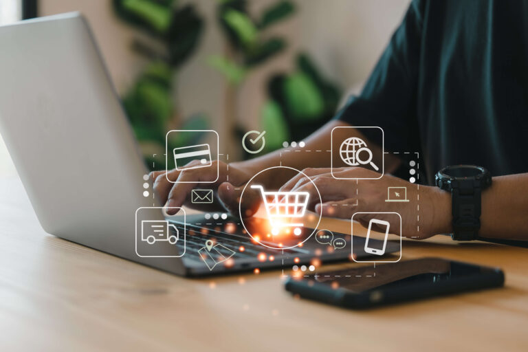 Hände an einem Laptop mit eingeblendeten E-Commerce-Symbolen wie Einkaufswagen, Kreditkarte und Versand-LKW.