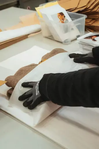 Hände mit Schutzhandschuhen schlagen hochwertige Textilien sorgfältig in weißes Seidenpapier ein.