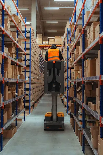 Blick durch einen hohen Regalgang im ONTARO Lager mit einem Mitarbeiter auf einer Hubarbeitsbühne bei der Kommissionierung.