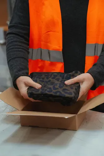 Logistikmitarbeiterin verpackt Kleidung in einem Karton.