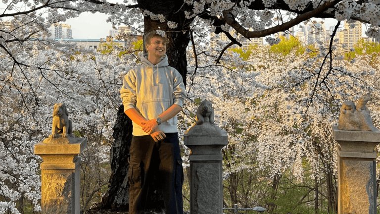 Ein Mann steht vor einem Baum mit weißen Blühten und lächelt.